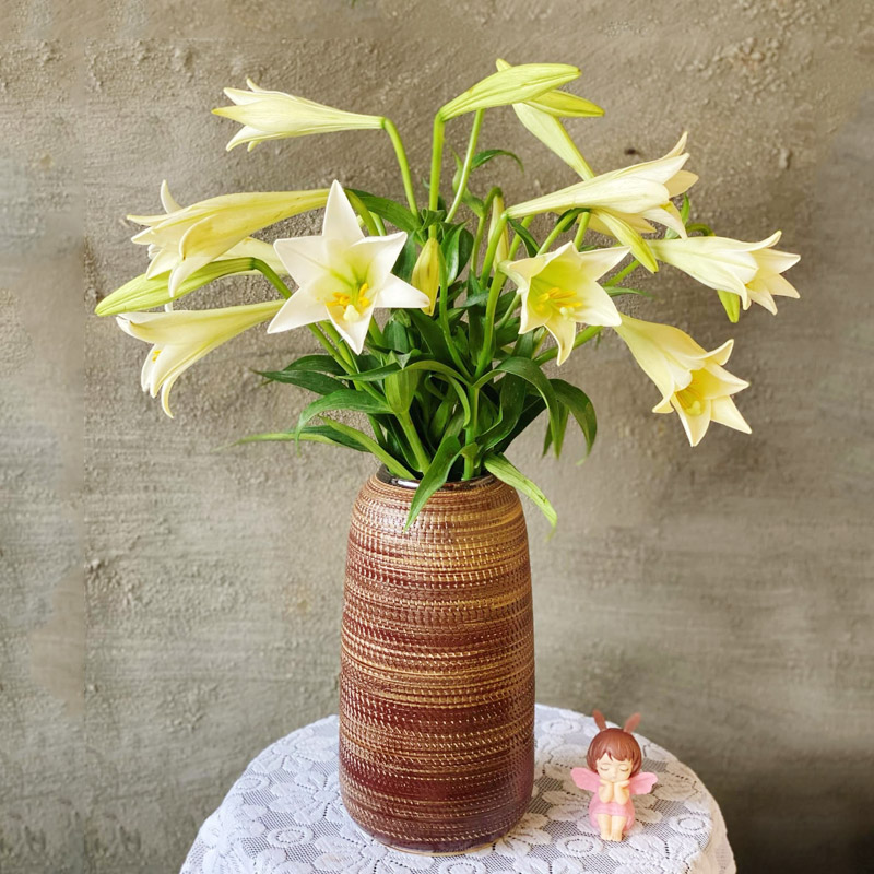 A cylindrical brown vase styled with white calla lilies for home decor